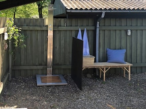 Eine Holzterrasse mit Metallkonstruktion, einer Bank mit Sitzkissen und einem überdachten Bereich mit Wellblechdach.