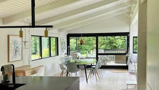 A modern kitchen with a large island, dining area with chairs, and a view of the outdoors through large windows. - Architect-designed 80s house by Hornbæk (Hornbæk)
