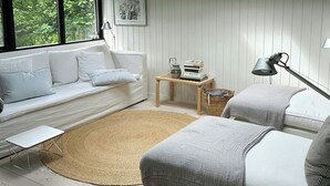 A modern bedroom with a skylight, white walls, a white sofa, a round rug, and a bedside table with books. - Architect-designed 80s house by Hornbæk (Hornbæk)