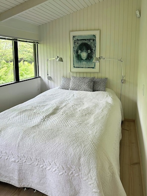 Ein Schlafzimmer mit einem großen Bett, einem gerahmten Bild an der Wand und einem Fenster mit Blick ins Grüne.