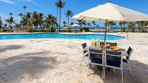Zona junto a la piscina con una mesa para dos, una sombrilla grande y vista al océano.