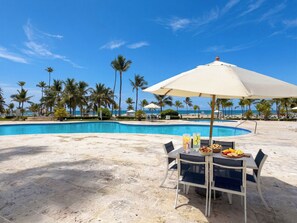 Ein Poolbereich mit einem Tisch für zwei Personen, einem großen Sonnenschirm und Blick auf das Meer.