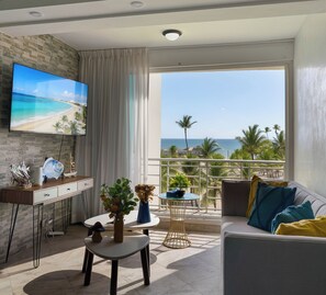 Ein Wohnzimmer mit Fernseher, einer Couch, einem Couchtisch und einem Balkon mit Meerblick.