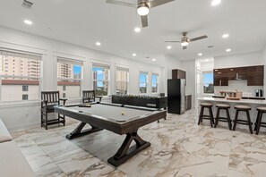 A spacious room with a pool table, bar stools, and a kitchen area. - Sleeps 44  + Pool + Spa | Theater + Game Room | Walk to Beach | Emerald Retreat (Destin)