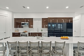 A modern kitchen with white cabinetry, a large island, stainless steel appliances, and a seating area with chairs. - Sleeps 44  + Pool + Spa | Theater + Game Room | Walk to Beach | Emerald Retreat (Destin)