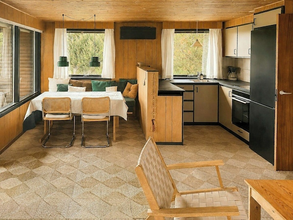 A compact kitchen with a dining area, wooden walls, and a large window. - Charming vintage house in North Sea nature (Ringkøbing)