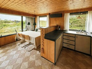 Una cocina compacta con comedor, techo de madera y ventanas amplias que dan a zonas verdes.