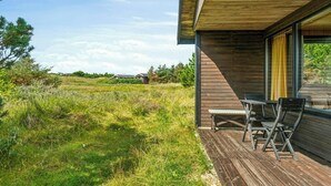 Eine Holterrasse mit Gartenmöbeln, freier Aussicht auf die umliegende Landschaft und ein modernes Gebäude mit großen Fenstern.