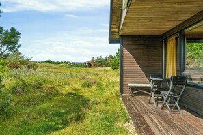 Eine Holterrasse mit Gartenmöbeln, freier Aussicht auf die umliegende Landschaft und ein modernes Gebäude mit großen Fenstern.