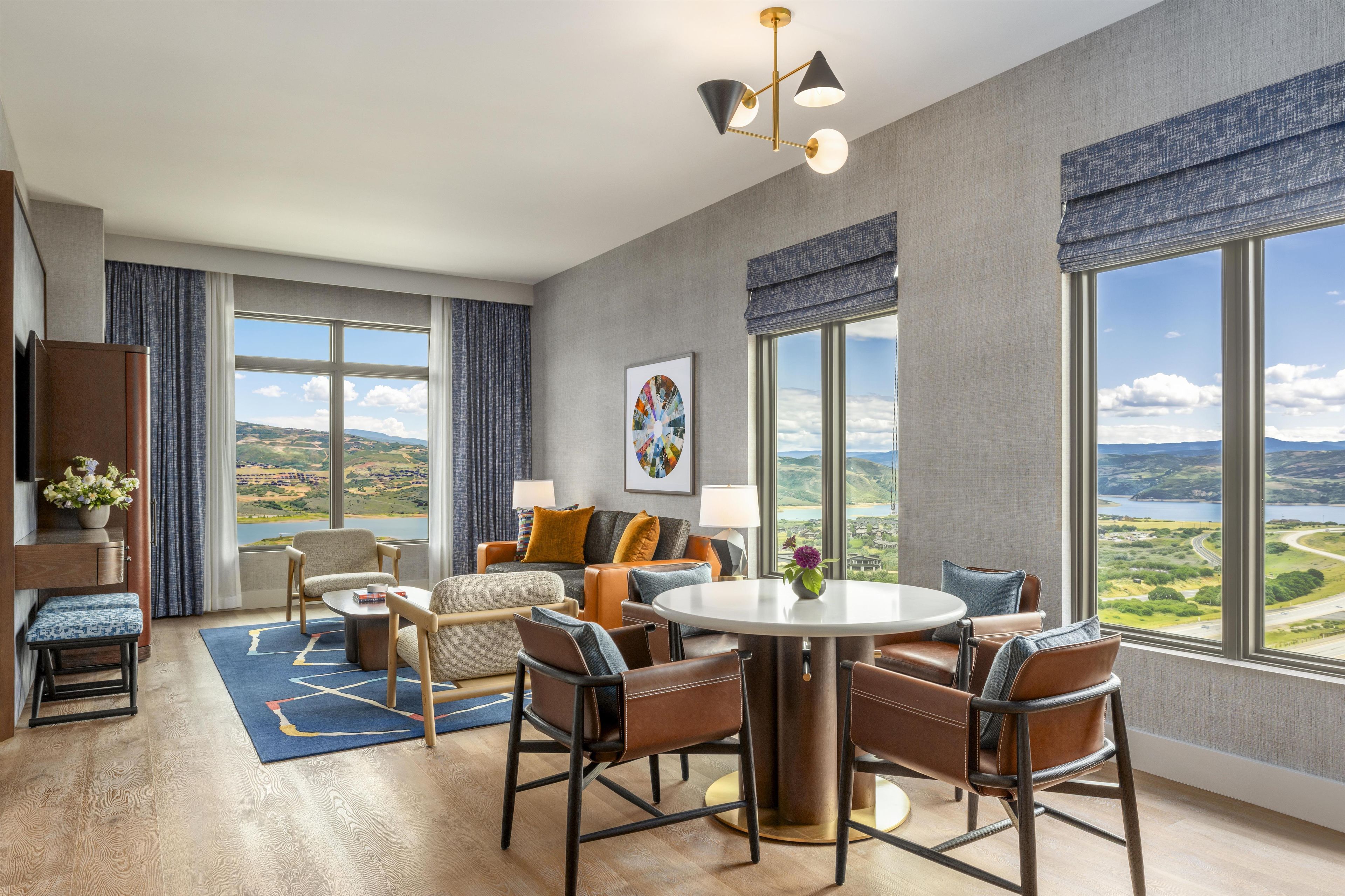 A modern hotel room with a large window, a round dining table, and a sofa.