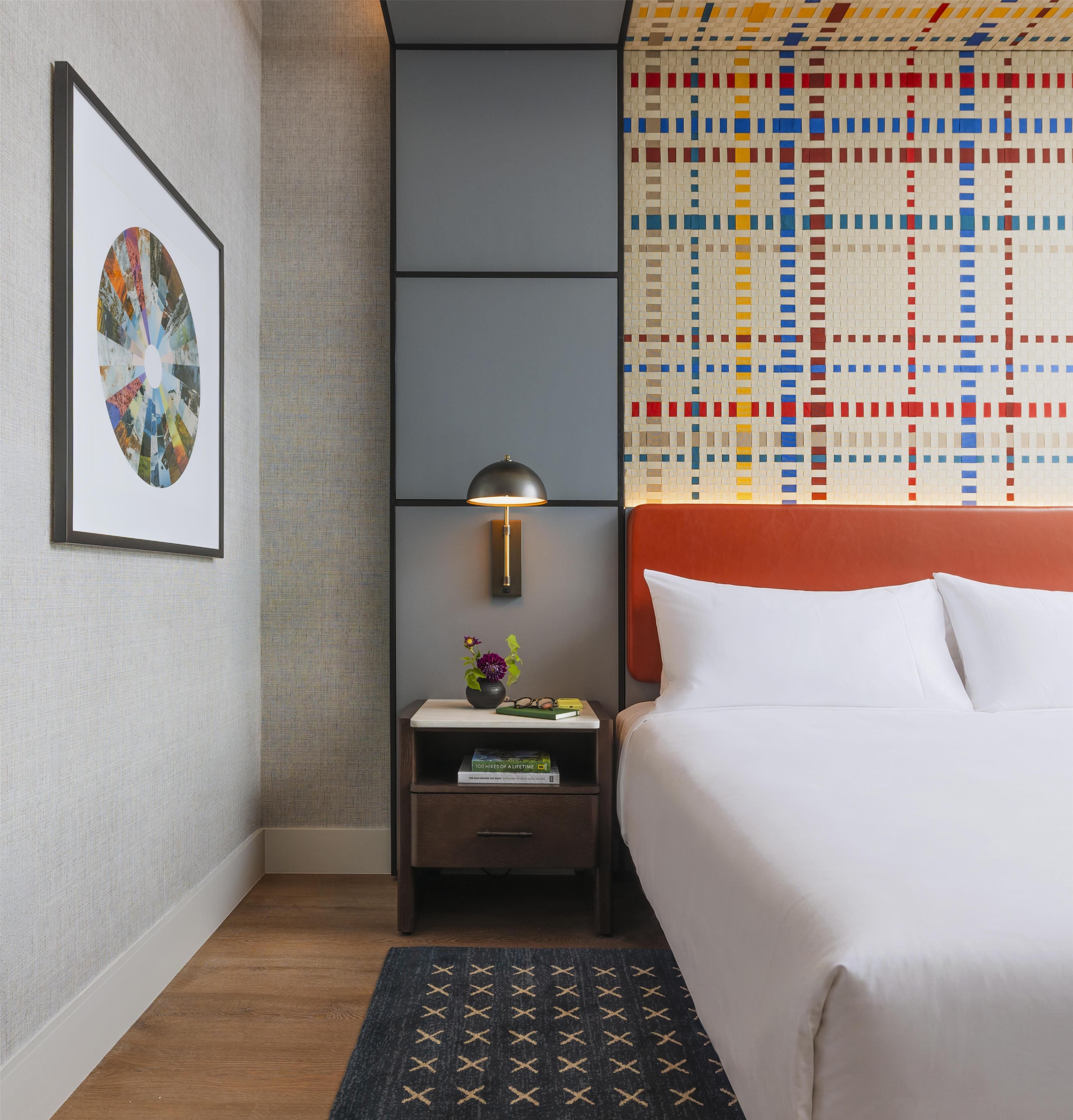 A hotel room with a bed, a nightstand, a framed artwork, a lamp, and a patterned wall.