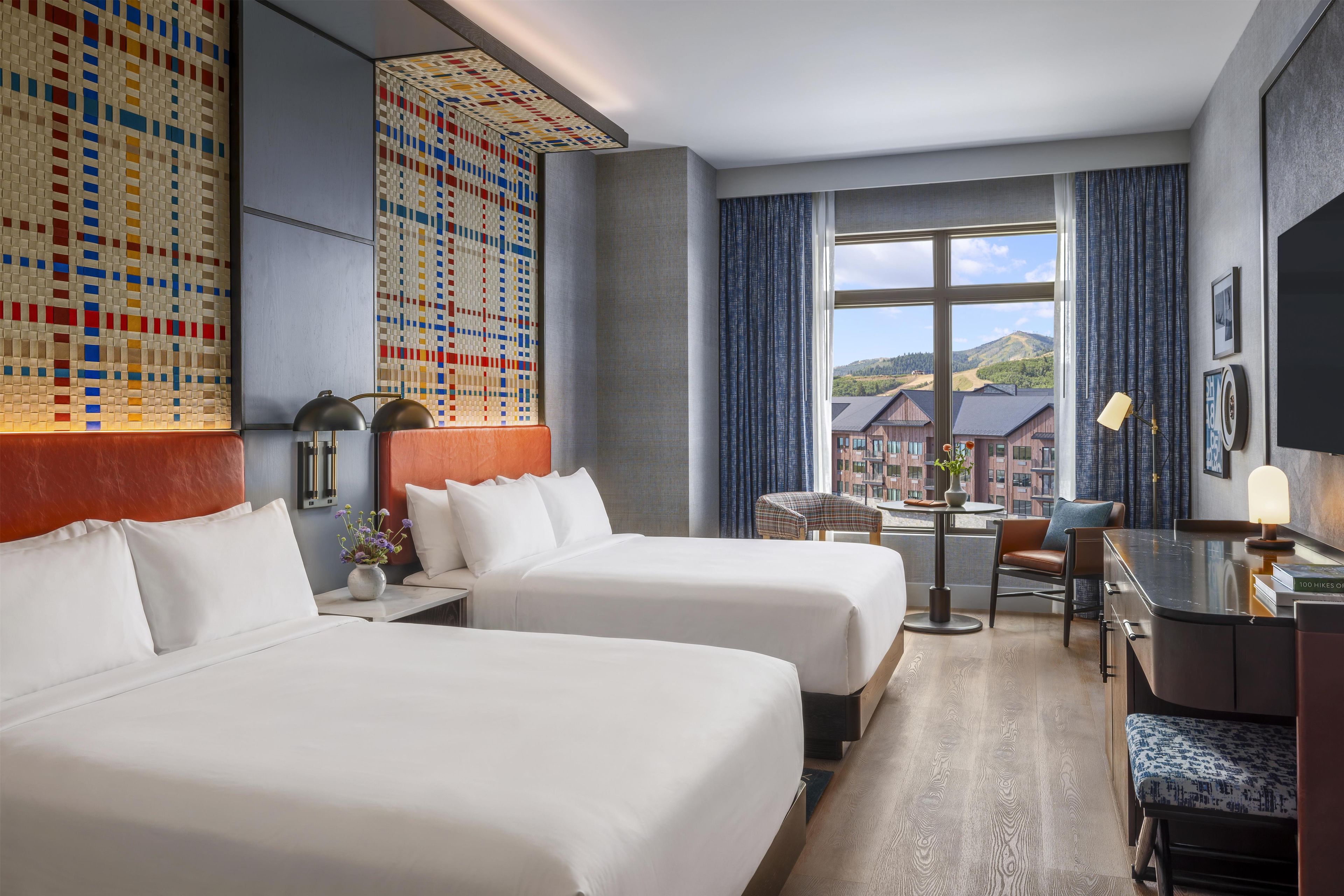 Une chambre d’hôtel avec deux lits, un bureau, une chaise, une vue sur l’extérieur et une grande fenêtre.