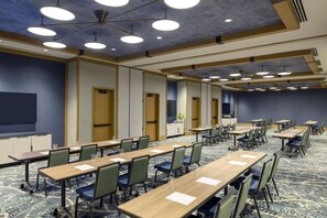 Un salón de conferencias con varias mesas y sillas, una pantalla grande e iluminación empotrada en el techo.