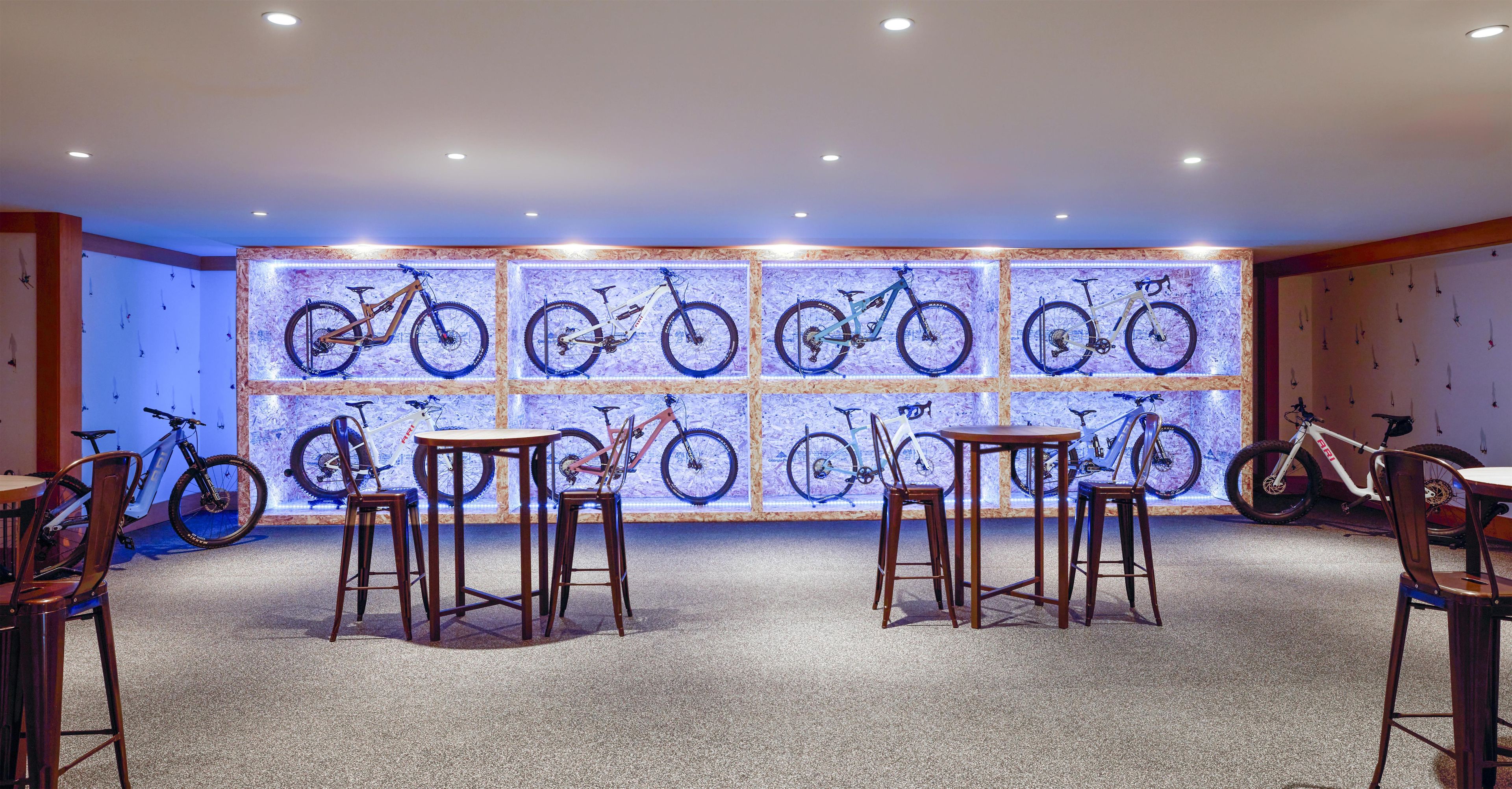 A room with a wall of illuminated bicycles, wooden furniture, and a carpeted floor.