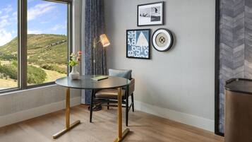 A room with a round table, a chair, a vase with flowers, a lamp, and framed pictures on the wall.
