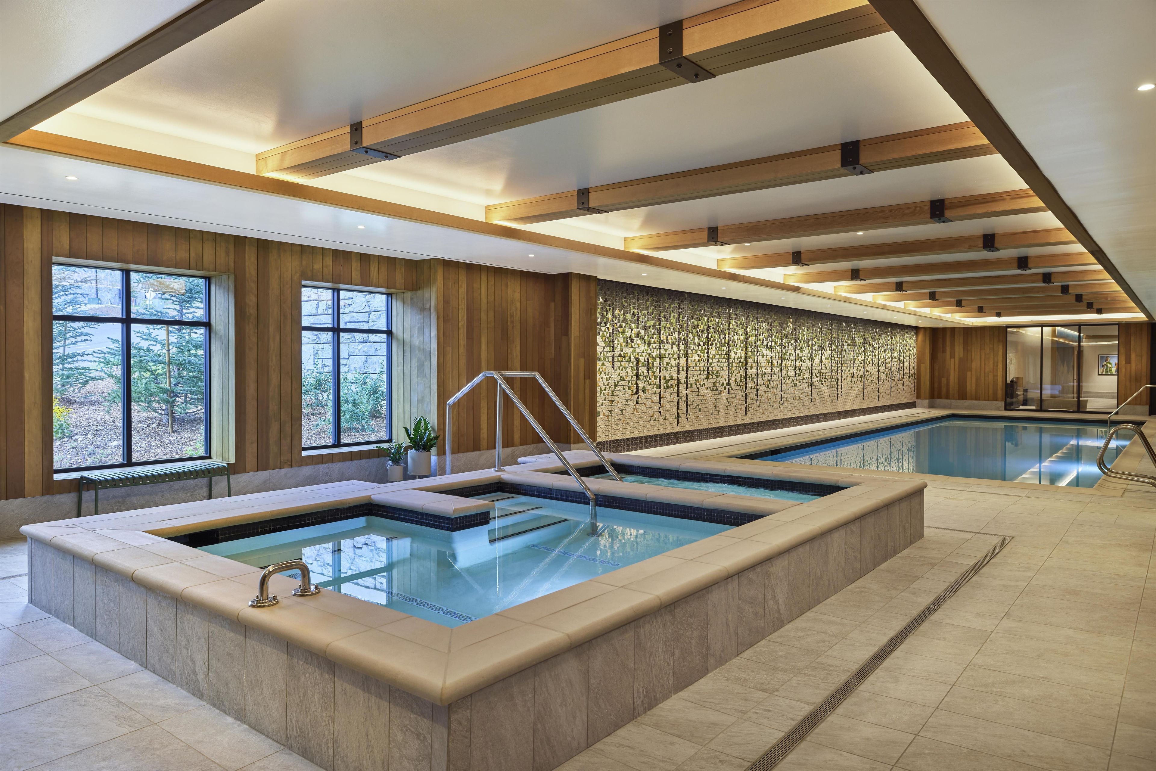A large indoor swimming pool with a wooden ceiling and a stone wall with a geometric pattern.