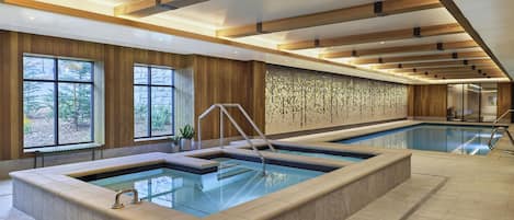 A large indoor swimming pool with a wooden ceiling and a stone wall with a geometric pattern.