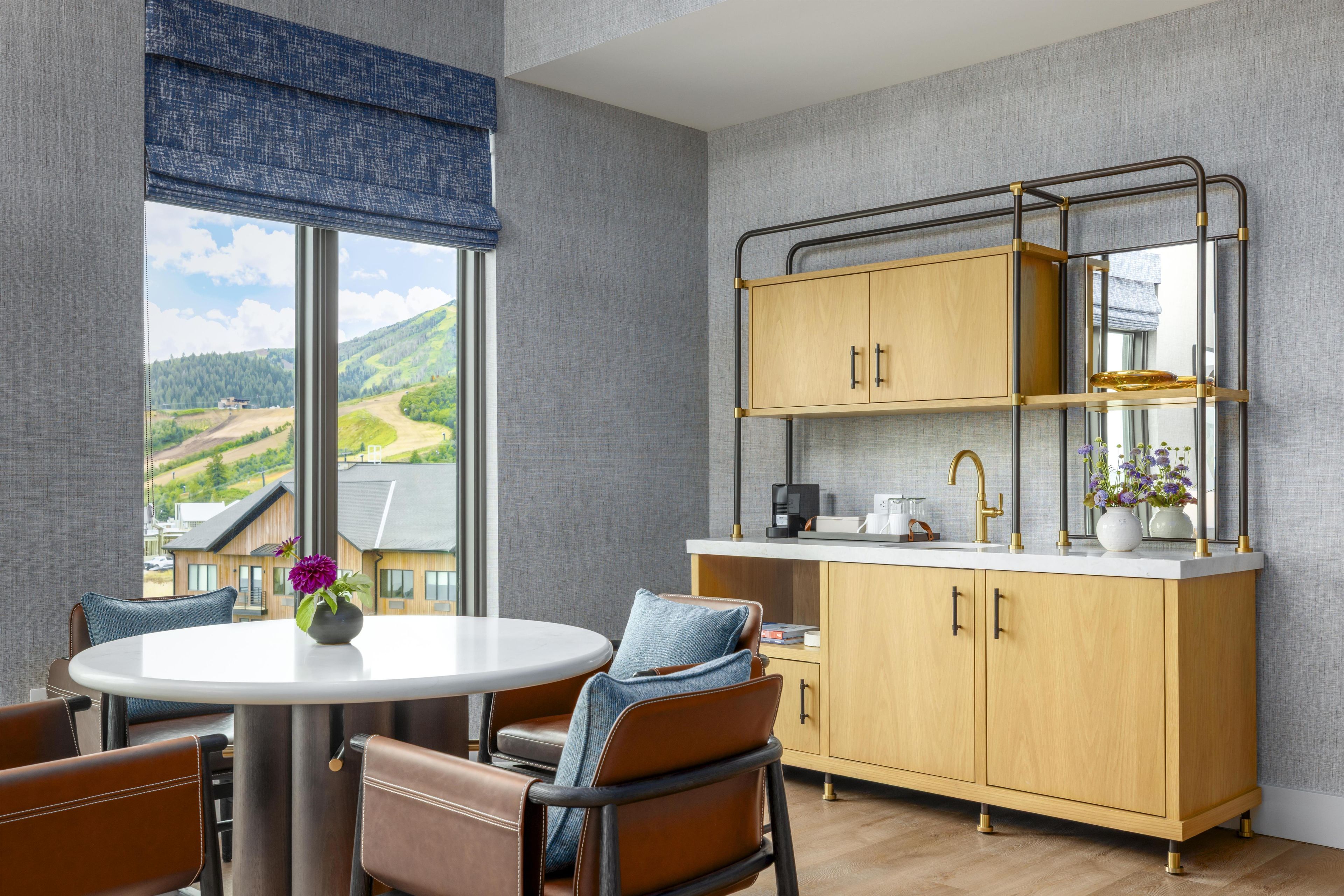 A modern kitchen with a view of a mountainous landscape, a round dining table with chairs, and a built-in bench.