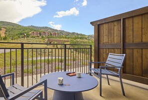 Un balcón con una mesa y sillas, una valla de madera y vistas a una zona residencial con casas en una colina.