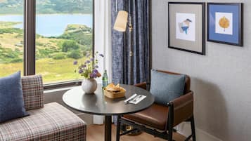 A room with a view of a lake, a dining table with a vase of flowers, and two framed pictures on the wall.