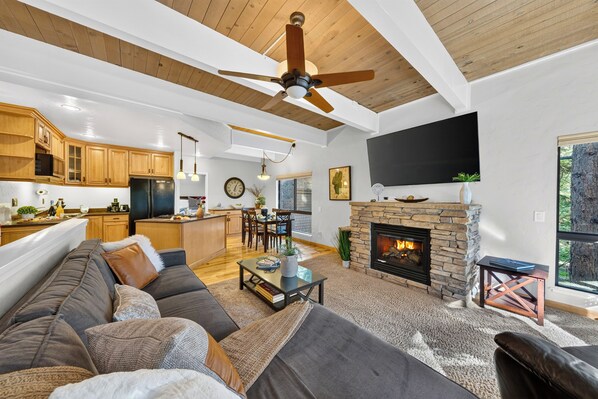 A modern living room with a fireplace, wooden ceiling, and a large TV mounted on the wall.
