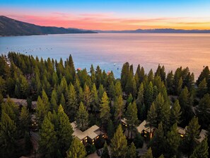 A resort with multiple cabins surrounded by dense forest, overlooking a large body of water and distant mountains.