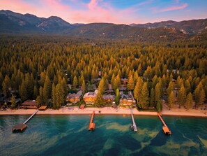 An aerial view of a coastal resort with multiple houses, a pier, and a forested backdrop.