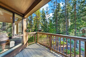 Eine Holzterrasse mit Glasgeländern mit Blick auf einen bewaldeten Bereich.