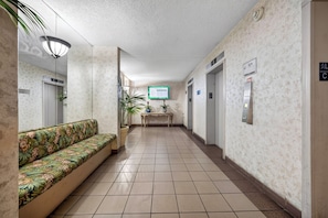 Eine Hotelhalle mit einer Bank, Blumentöpfen, einer Rezeption und Aufzugsschildern.