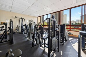 Ein Fitnessstudio mit verschiedenen Trainingsgeräten, großen Fenstern und Blick auf Gebäude.