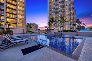 A rooftop pool with lounge chairs, a swimming pool, and high-rise buildings in the background. - Oceanview Condo + Pool + Gym | 10-Min Walk to Beach | Coastal Getaway Waikiki (Honolulu)