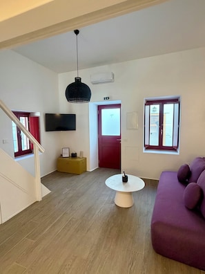 Ein modernes Wohnzimmer mit Treppe, Flachbildfernseher, rundem Couchtisch und einem violetten Sofa.