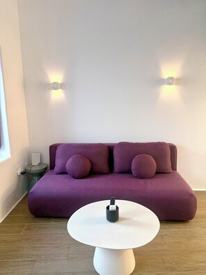 Ein violettes Sofa mit runden Kissen, ein weißer runder Tisch und zwei Wandleuchten.