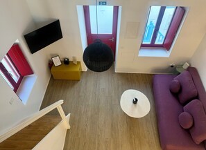 Ein modernes Zimmer mit einer Couch, einem kleinen Tisch, einem an der Wand montierten Fernseher, einer roten Tür und einem Fenster mit Blick.