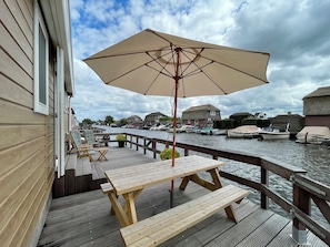 Eine Holzterrasse mit Tisch und Bank, mit Blick auf einen Kanal und Boote.