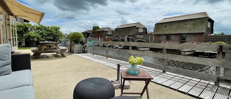 A patio with outdoor seating, a wooden table with a vase, and a view of water and traditional houses.