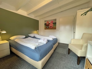 Ein Hotelzimmer mit Bett, Nachttisch, Lampe, Stuhl und einer Tür.