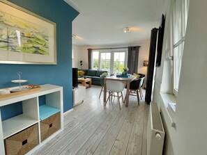 A modern living room with a dining area, a sofa, a TV, and a window with curtains. - Luxury holiday home for 6 guests featuring a spacious waterfront terrace, a private swimming ladder, and its own mooring dock. (Breukelen)