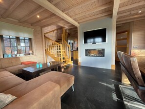 A spacious living area with a wooden staircase, a fireplace, and a flat-screen TV mounted on the wall. - 4-person holiday home on a small-scale holiday park with infrared sauna and beautiful views in a quiet area (Den Ham)