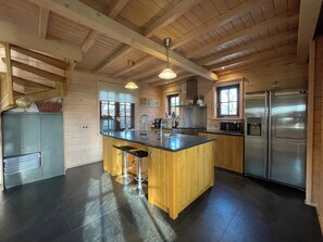 A kitchen with wooden beams, a central island with stools, stainless steel appliances, and a view of the outdoors through windows. - 4-person holiday home on a small-scale holiday park with infrared sauna and beautiful views in a quiet area (Den Ham)