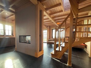 A spacious room with a wooden staircase, a fireplace, and a large window. - 4-person holiday home on a small-scale holiday park with infrared sauna and beautiful views in a quiet area (Den Ham)