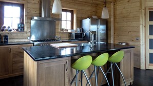 Une cuisine avec des murs en bois, des appareils électroménagers en acier inoxydable, un plan de travail noir et des tabourets de bar verts.