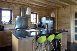 Eine Küche mit Holzwänden, Edelstahlgeräten, einer schwarzen Arbeitsplatte und grünen Barhocker.