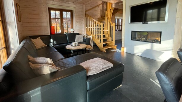 Un salon moderne avec un canapé en cuir noir, un escalier en bois et une cheminée.