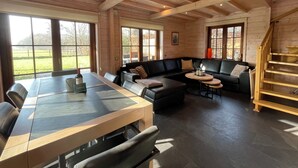 Une pièce spacieuse avec un plafond en bois, de grandes fenêtres, un canapé en cuir noir, une table à manger et un escalier.