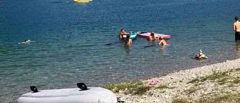 En sjö med båtar, folk som badar och en grönskande strand.