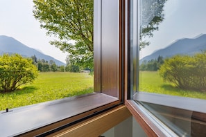 Ein Fenster mit Blick auf ein grünes Feld und Berge.