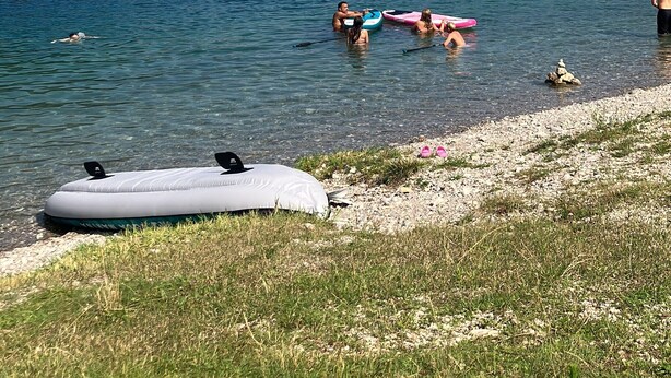 Ein See mit Booten, badenden Personen und einem grasbewachsenen Ufer.