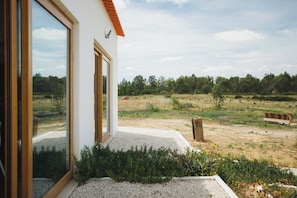 A modern house with large windows, a gravel patio, and a view of a grassy field.