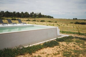 A swimming pool with lounge chairs, surrounded by a grassy field and trees.